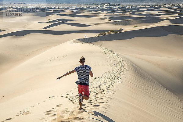 Junger Mann  Tourist läuft eine Sanddüne hinunter  Mesquite Flat Sand Dunes  Sanddünen  Death Valley  Death-Valley-Nationalpark  Kalifornien  USA  Nordamerika