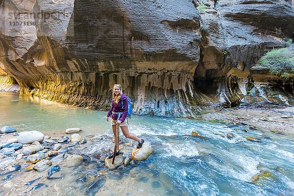 Wanderin überquert Fluss auf Steinen  Zion Narrows  Engstelle des Virgin River  Steilwände des Zion Canyon  Zion Nationalpark  Utah  USA  Nordamerika