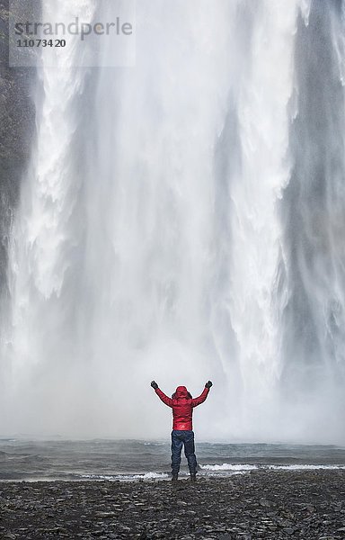 Wanderer mit ausgestreckten Armen vor Wasserfall Skogafoss im Winter  Skógar  Südisland  Island  Europa