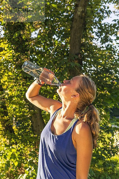 Junge Frau in Sportkleidung trinkt Wasser aus einer Flasche  Bayern  Deutschland  Europa