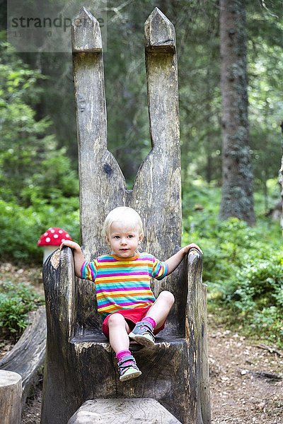 Kleinkind sitzt auf einem großen Stuhl aus Holz im Wald  Zauberwald bei Bernau  Schwarzwald  Deutschland  Europa