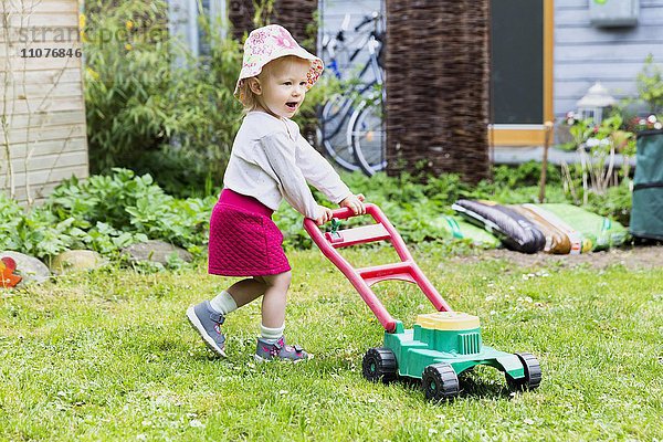 Kleinkind  kleines Mädchen im Garten mit Spielzeug-Rasenmäher
