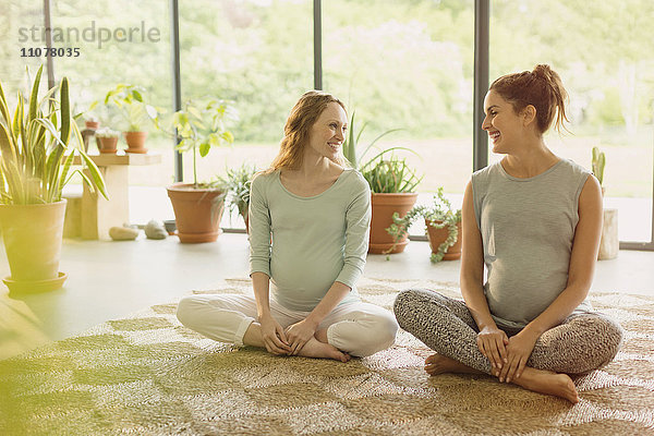 Lächelnde schwangere Frauen sprechen auf dem Teppich