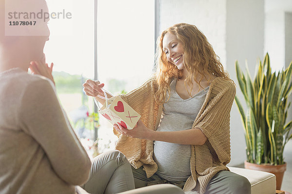 Lächelnde schwangere Frau erhält ein Geschenk von einem Freund