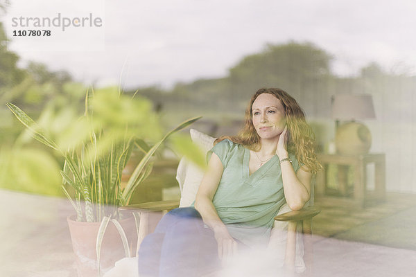 Nachdenkliche Frau mit Blick aus dem Wohnzimmerfenster