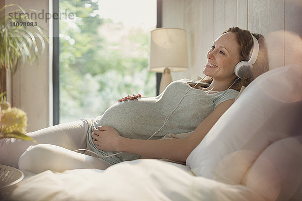 Lächelnde Schwangere entspannt Musik hören mit Kopfhörern im Bett