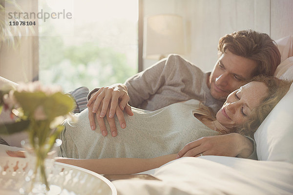 Ein ruhiges  schwangeres Paar  das den Bauch auf dem Bett hält.