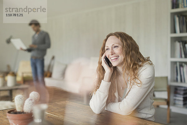 Lächelnde Frau beim Telefonieren am Esstisch