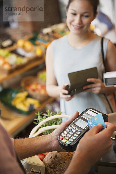 Frau beobachtet die Verkäuferin eines Lebensmittelgeschäfts mit einem Kreditkartenautomaten.