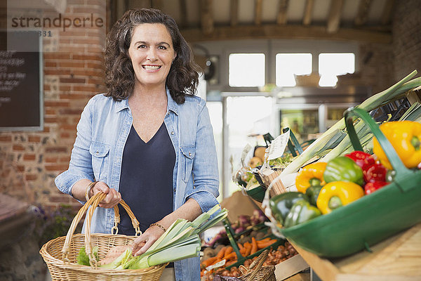 Portrait lächelnde Frau mit Einkaufskorb für Produkte auf dem Markt