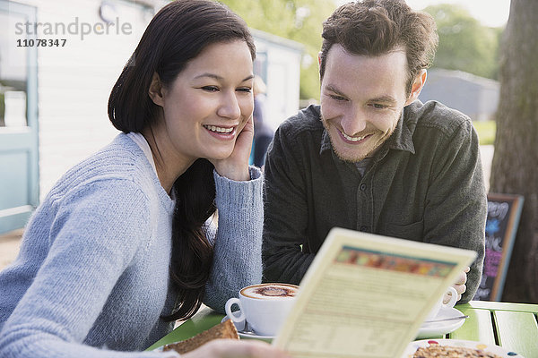 Lächelndes Paar beim Lesen des Menüs im Outdoor-Café