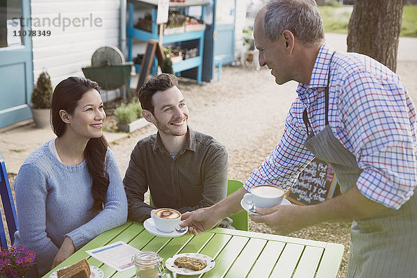 Kellner serviert Cappuccinos für ein lächelndes Paar in einem Outdoor-Café