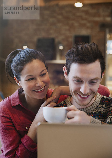 Lächelndes Paar trinkt Cappuccino am Laptop im Cafe