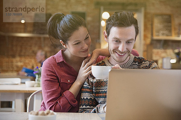 Lächelndes Paar beim Kaffeetrinken mit Laptop im Café