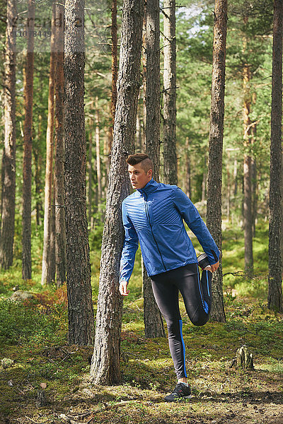 Läufer streckt Bein am Baum im Wald