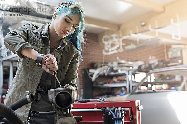 Junge Mechanikerin mit blauen Haaren in der Autowerkstatt