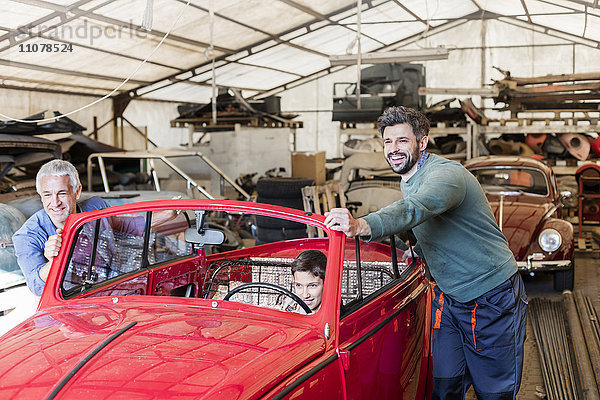 Lächelnde Mechaniker schieben Jungen im Oldtimer in Autowerkstatt
