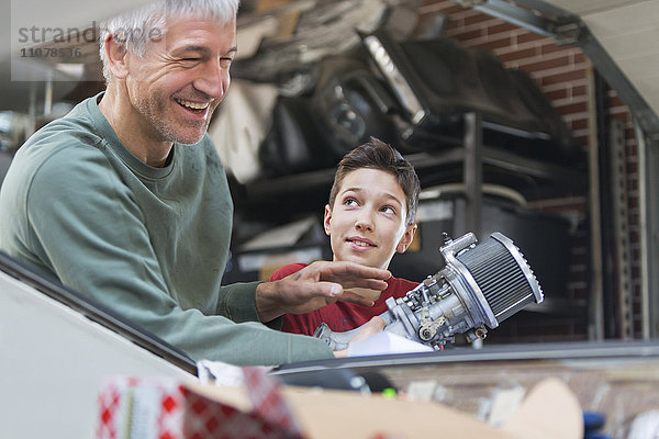 Lächelnder Vater und Sohn beim Reparieren des Motors in der Autowerkstatt