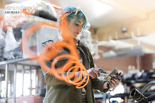 Junge Mechanikerin mit blauen Haaren mit Geräten in der Autowerkstatt