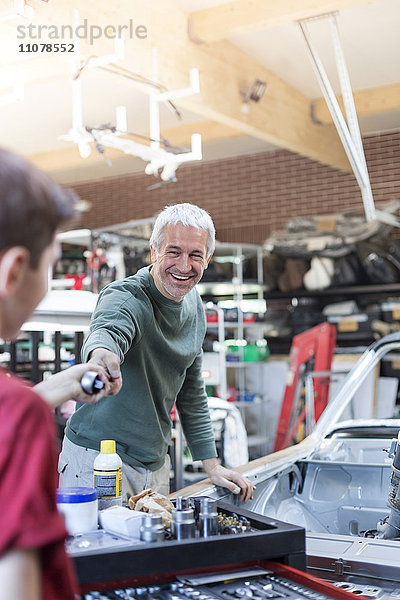 Lächelnder Vater nimmt Werkzeug vom Sohn in der Autowerkstatt