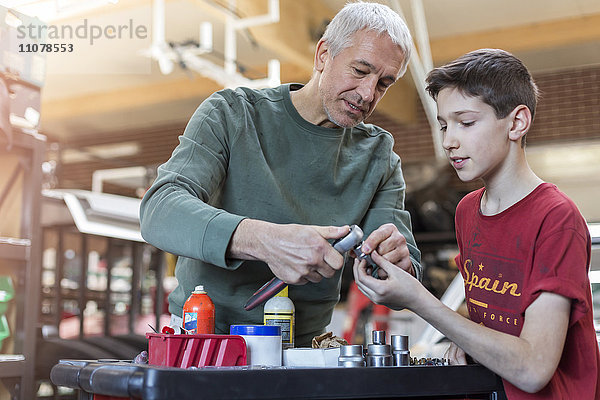 Vater lehrt Sohn  wie man Werkzeuge in der Autowerkstatt benutzt.