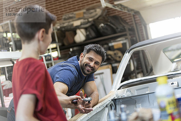 Lächelnder Vater nimmt Werkzeug vom Sohn in der Autowerkstatt