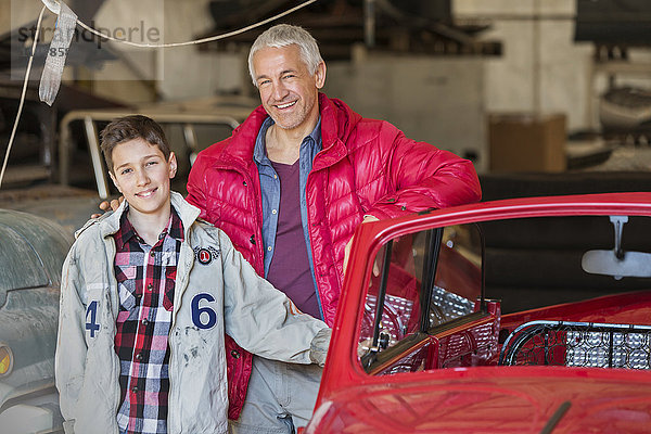 Portrait lächelnder Vater und Sohn neben dem Oldtimer in der Autowerkstatt