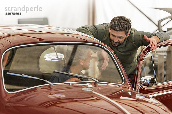 Mechaniker im Gespräch beim Oldtimer in der Kfz-Werkstatt