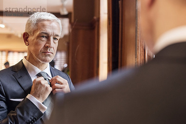 Geschäftsmann beim Anprobieren des Spiegels im Herrenausstattergeschäft