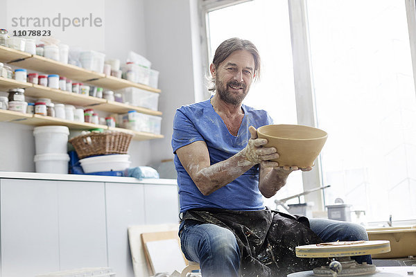 Porträt selbstbewusster reifer Mann hält Schale an Töpferscheibe im Atelier