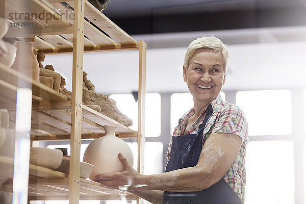 Lächelnde Seniorin stellt Keramikvase im Studio ins Regal