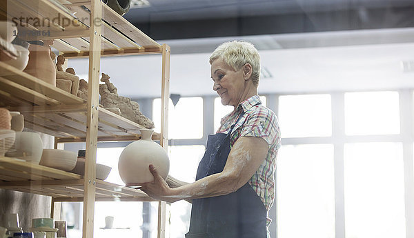 Seniorenfrau stellt Keramikvase ins Regal im Atelier