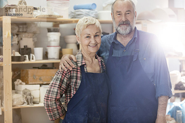 Portrait lächelndes Seniorenpaar mit Schürzen im Töpferatelier