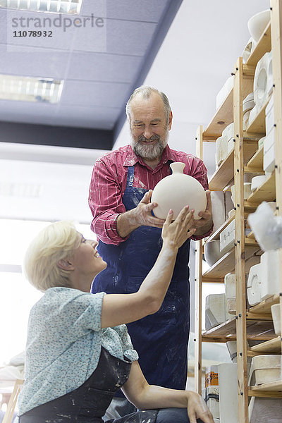 Lächelndes Paar stellt Keramikvase ins Regal im Atelier