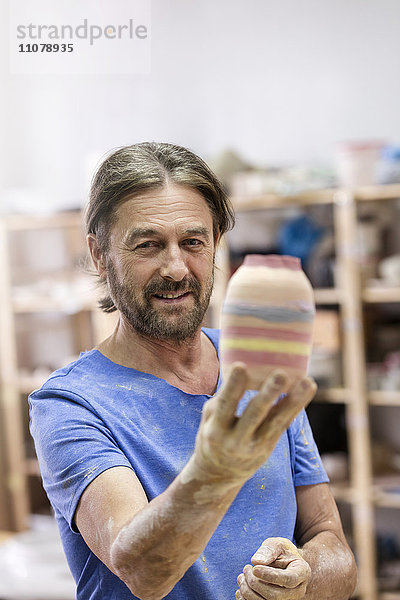 Portrait lächelnder reifer Mann mit bemalter Keramikvase im Atelier