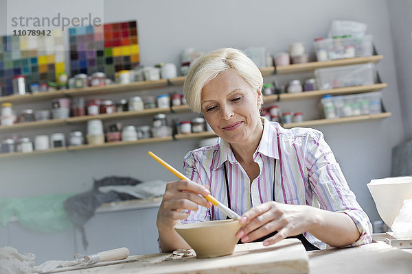 Lächelnde reife Frau malt Töpferschale im Atelier