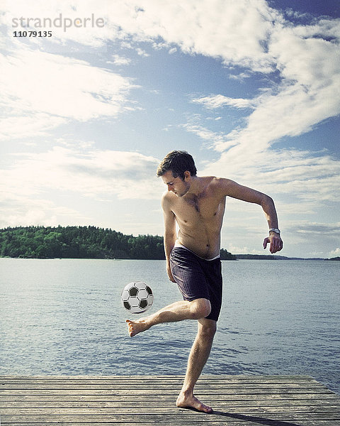 Junger Mann spielt mit Fußball auf dem Steg