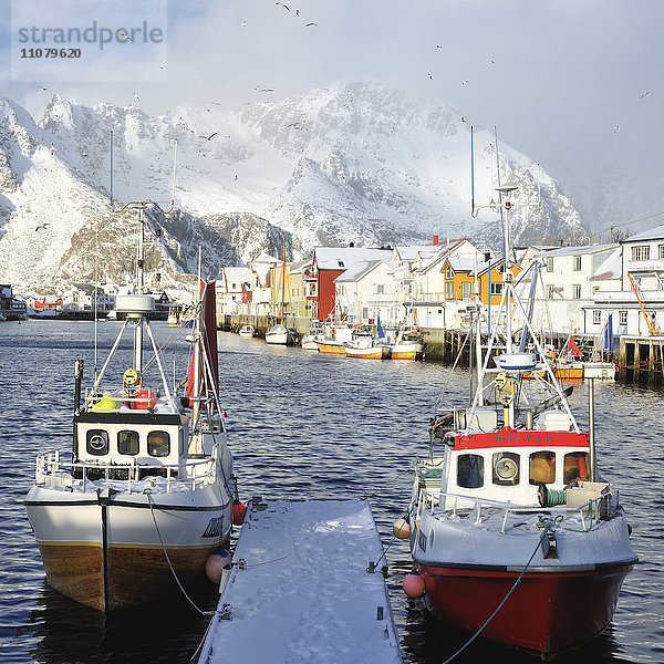 Fischerboote an der Anlegestelle  Dorf und schneebedeckte Berge im Hintergrund