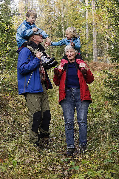 Großeltern tragen Enkelkinder auf den Schultern im Wald