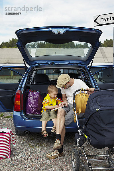 Vater mit Sohn liest im Kofferraum eines Autos