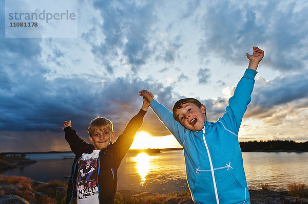 Zwei Jungen stehen bei Sonnenuntergang am Strand