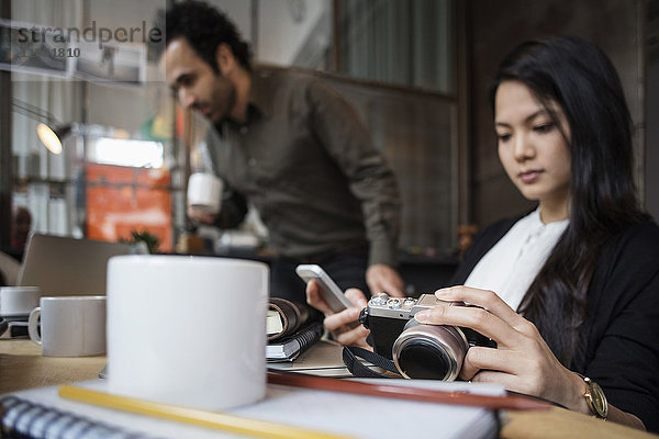 Geschäftsfrau mit Kamera und Telefon mit Kollegin im Hintergrund im Kreativbüro