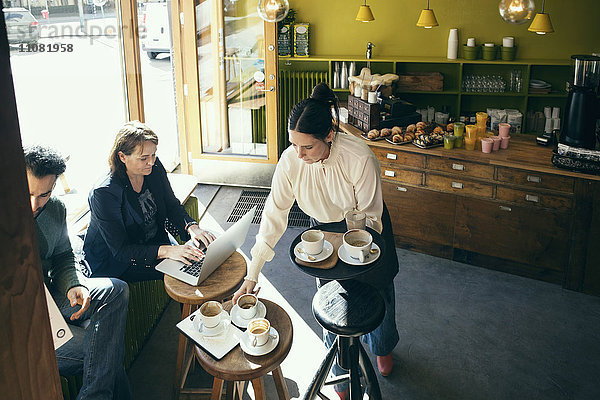 Hoher Blickwinkel auf die Barista beim Aufnehmen von Kaffeetassen  während die Kunden am Tisch sitzen.