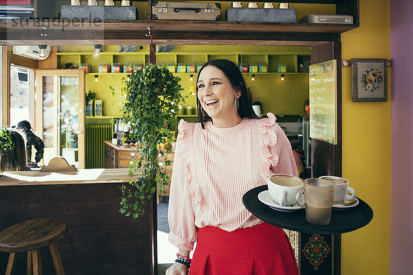 Fröhliche Kellnerin hält Serviertablett  während sie im Café wegschaut