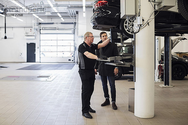 Senior-Mechaniker erklärt den Kunden im Werkstattbetrieb