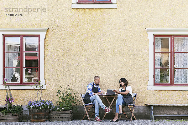 Mann und Frau diskutieren über das digitale Tablett  während sie am Tisch vor dem Café sitzen.