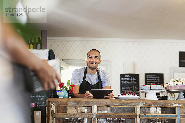 Lächelnder Bäcker mit digitalem Tablett beim Anblick einer Kollegin im Café