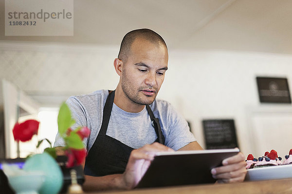 Männlicher Besitzer mit digitalem Tablett am Cafe-Schalter