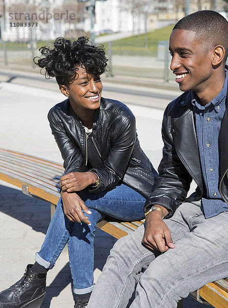 Lächelndes junges Paar sitzt auf einer Bank