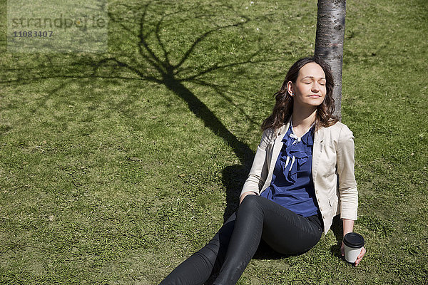 Junge Frau sitzt unter einem Baum  Stockholm  Schweden
